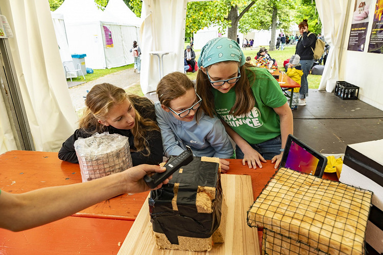Drei Mädchen bei einer Mitmachstation von Explore Science betrachten gemeinsam ein Dämmmaterial-Experiment zur Wärmedämmung.